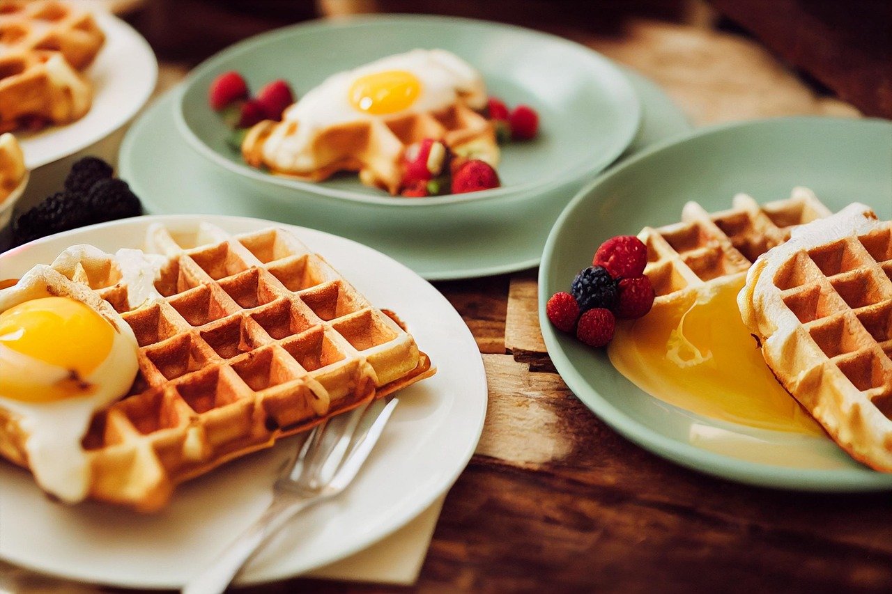 A restaurant table with three plates containing waffles, eggs, and berries.